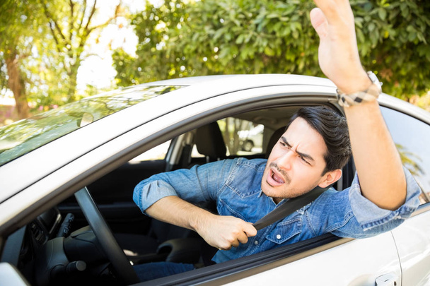 Portrait of angry young man sitting in his car shouting and gesturing at other drivers during traffic on road - Foto, Bild