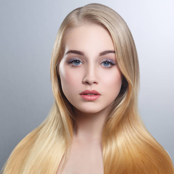 Beauty portrait of a cute blonde with long straight hair isolated groomed on a gray background. - Valokuva, kuva