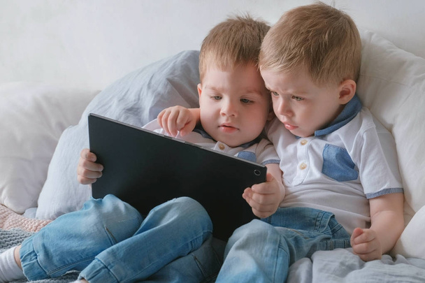 Kids with tablet. Two boys twins toddlers looking cartoon at tablet lying on the bed. - Fotoğraf, Görsel