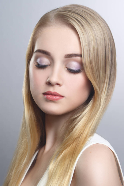 Beauty portrait of a cute blonde with long straight hair isolated groomed on a gray background. - 写真・画像