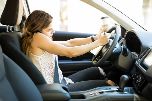 美しい若い女性のコーヒー カップを保持している、電話で話していると車を運転している間ノートを作って - 写真・画像