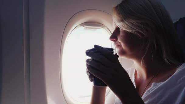 A woman is drinking coffee in the cabin of an airplane. Sits by the window - Video, Çekim