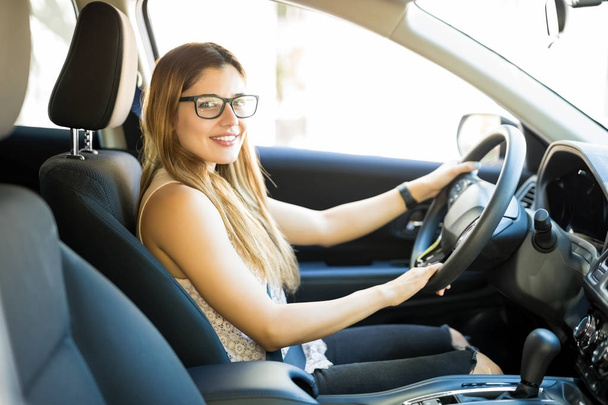 hübsche junge kaukasische Frau sitzt auf dem Fahrersitz ihres Autos und nimmt Blickkontakt auf - Foto, Bild