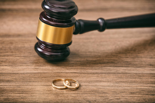 Divorce concept. Wedding rings and judge gavel on wooden background, copy space - Фото, изображение