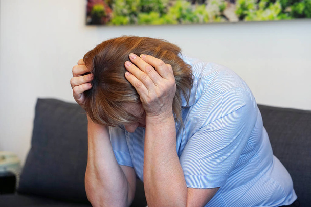 Starsza kobieta cierpi na ból głowy Migrena ból w domu. Problem zdrowotny, stres i depresja. Kobieta trzyma głowę ręką. Pojęcie zdrowia. - Zdjęcie, obraz