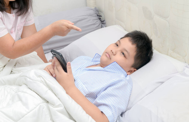 Anya elrendelte, hogy gyermekek ne játszanak mobiltelefonok hosszú ideig ágyban, egészségügyi koncepció probléma - Fotó, kép