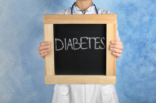 Doctor holding chalkboard with word DIABETES on color background - Photo, Image