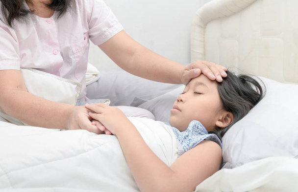 Mother measuring temperature of her ill kid. Sick girl with thermometer laying on bed and mother hand taking temperature. Sick child with fever and illness in bed - Foto, Bild