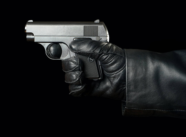 Gun in the hand of a bandit wearing gloves on a black background - Фото, изображение