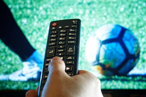 La main de la personne tient la télécommande de télévision pendant la diffusion du match de football
    - Photo, image
