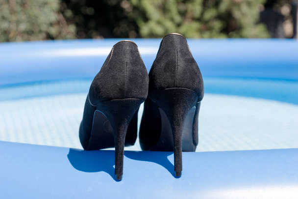 Beautiful black high heels on the edge of the swimming pool - Photo, Image