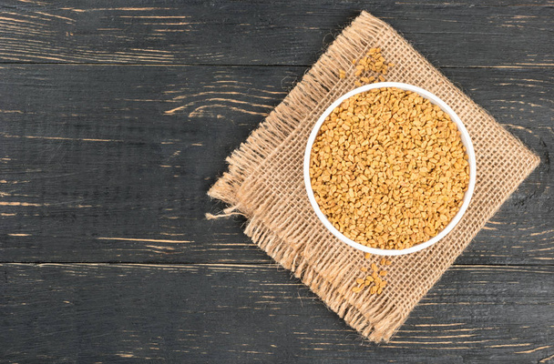 Bowl with fenugreek beans on burlap and empty wooden background - Photo, Image