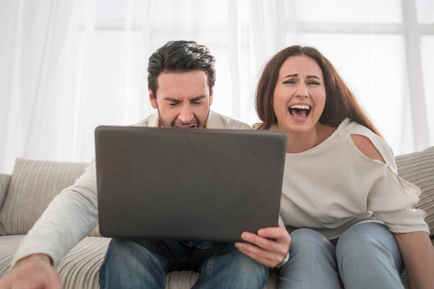 Happy couple sitting on sofa and using laptop at home - Foto, imagen