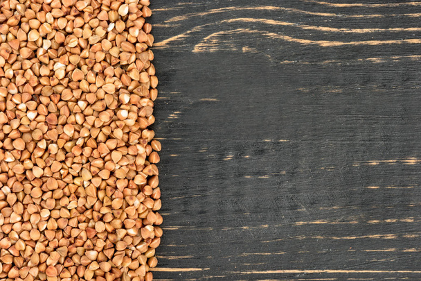 Raw grains of buckwheat on an empty wooden background - Valokuva, kuva