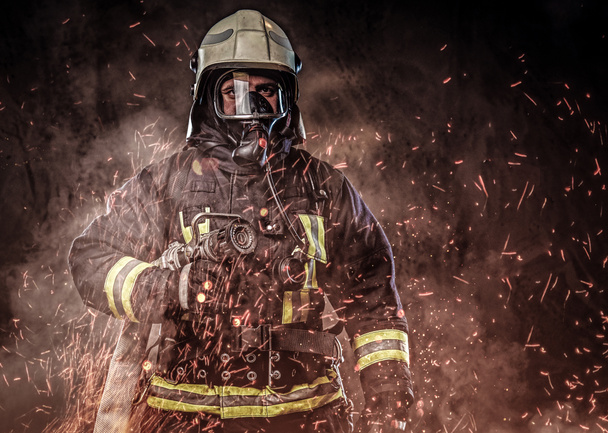 プロの消防士の制服を着て、火で酸素マスクの立っている火花し煙の黒っぽい背景に. - 写真・画像