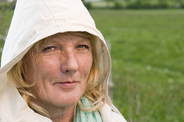 Portrait de tête latéral d'une femme blonde d'âge moyen devant une prairie verte regardant joyeusement dans la caméra
. - Photo, image