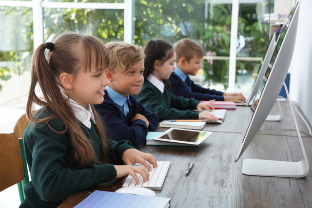 Little children in stylish school uniform at desks with computers - Fotoğraf, Görsel
