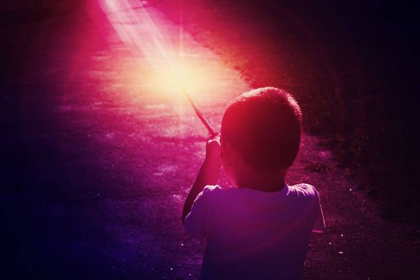 chłopiec z różdżką w ręku pokazuje magia na tle ciemno fioletowy neon - Zdjęcie, obraz