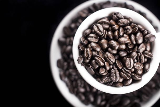 Black coffe beans in white cup and plate on dark background. Close up. - Foto, Bild