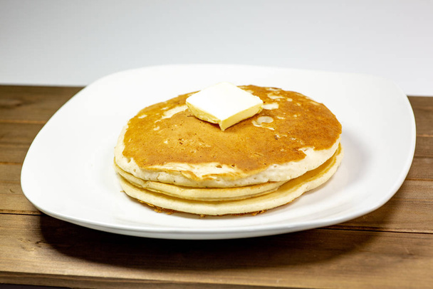 Ένα τετράγωνο βούτυρο τοποθέτηση επάνω σε μια στοίβα από pancakes χρυσή στο τραπέζι της κουζίνας, περιμένοντας να καταναλωθούν - Φωτογραφία, εικόνα