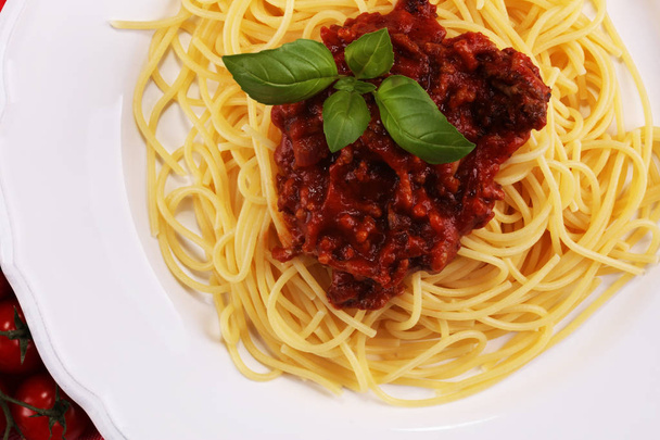 Тарелка вкусных спагетти Болоньез или Болоньезе с мясной говядиной и томатным соусом, украшенным сыром пармезан и базиликом
 - Фото, изображение