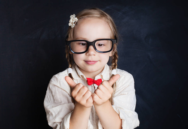 Funny child on blackboard background. Happy smiling girl in glasses with thumb up. Back to school. - Фото, зображення