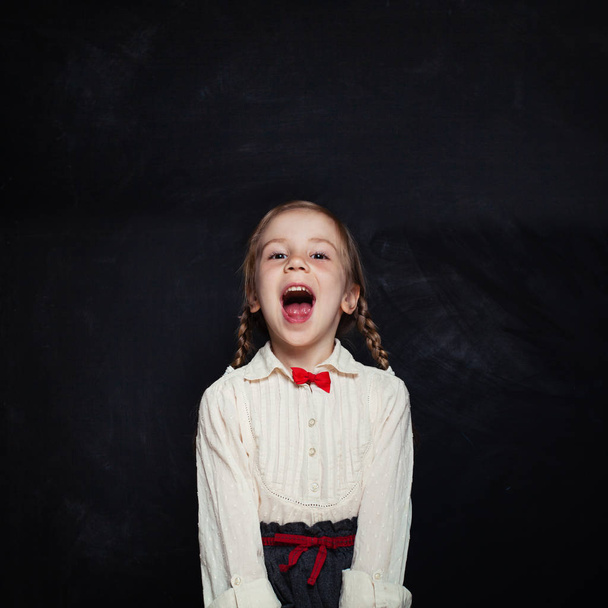 笑いや楽しい幸せな子の女の子。コピー スペースを持つ空の黒板背景に制服の学校の子供の笑みを浮かべてください。学校に戻る. - 写真・画像