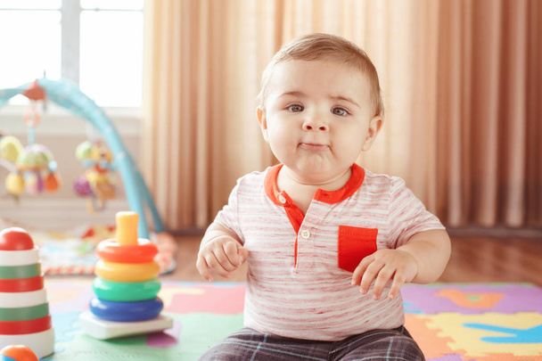Closeup retrato de bonito adorável loiro caucasiano sorridente menino com olhos azuis sentado no chão na sala de crianças. Bebé brincando com brinquedos no playmat. Desenvolvimento da educação inicial
 - Foto, Imagem