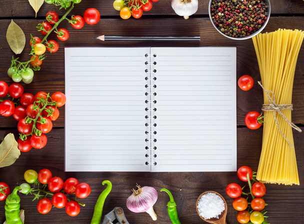 open blank notebook in a line and a black wooden pencil and ingredients for cooking Italian pasta, vegetables and spices - Photo, Image