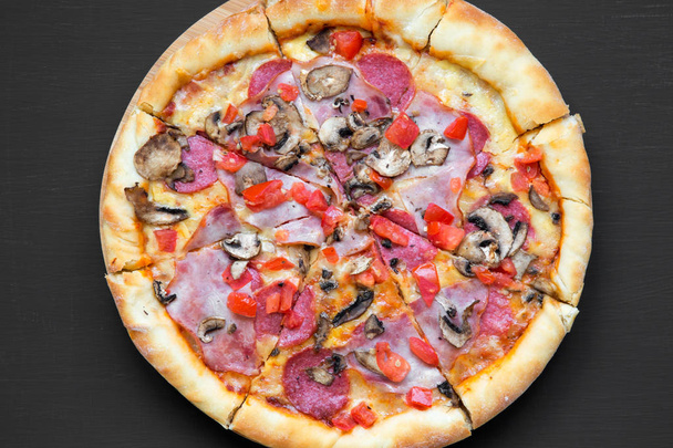 von oben, frisch gebackene Pizza auf schwarzer Oberfläche. Draufsicht, flach liegend, über Kopf. Nahaufnahme. - Foto, Bild