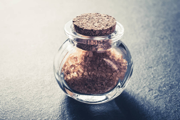 Κλειστό γκρο πλαν του μια καφέ ακατέργαστη ζάχαρη σε ένα μικρό γυάλινο μπουκάλι με πώμα φελλού σε σχιστόλιθο πέτρα - Φωτογραφία, εικόνα