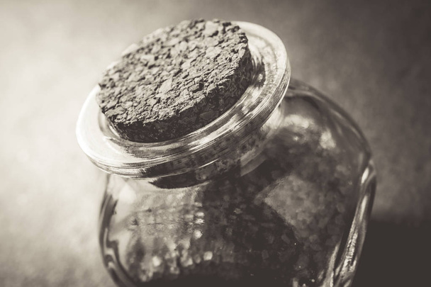 Macro Of A Brown Raw Sugar In A Small Glass Bottle Closed With A Cork Stopper On Slate Stone In Monochrome Colors - Foto, imagen