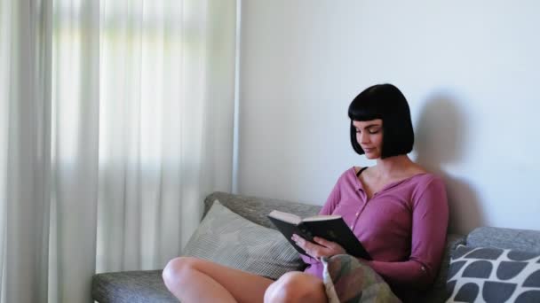Woman reading a novel in living room at home 4k - Video, Çekim