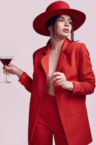 Portrét elegantní krásné ženy v červené módní oblek a široký klobouk s alkoholem koktejl izolovaných na bílém pozadí v studio - Fotografie, Obrázek