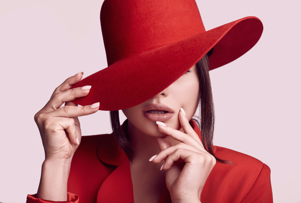 Portrait of elegant beautiful woman in a red fashionable suit and wide hat isolated on white background in studio - Photo, Image