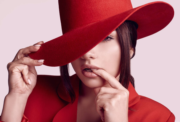 Portret van elegante mooie vrouw in een rood trendy pak en de brede hoed, geïsoleerd op een witte achtergrond in de studio - Foto, afbeelding
