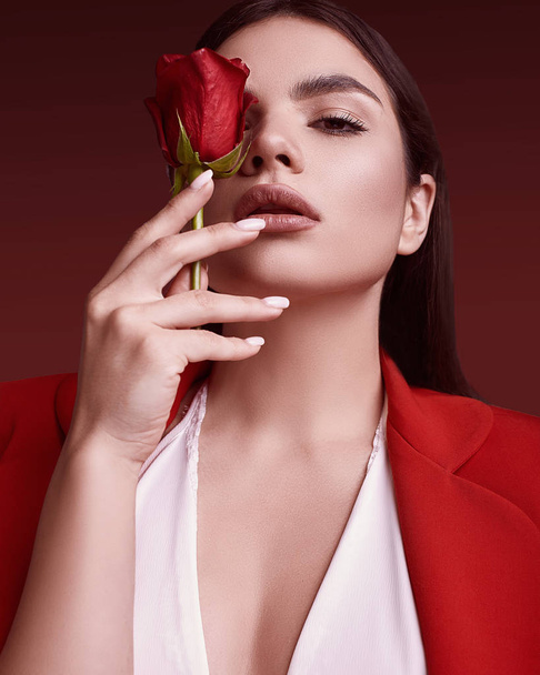 スタジオでカラフルな背景のバラと赤いおしゃれなスーツでエレガントな美しい女性の肖像画 - 写真・画像