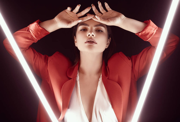 Portrait of elegant beautiful woman in a red fashionable suit posing around glowing neon lights - Photo, Image