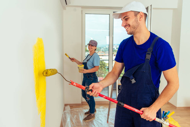 Молода пара малює стіну вдома жовтим кольором з пензлем і фарбою
 - Фото, зображення
