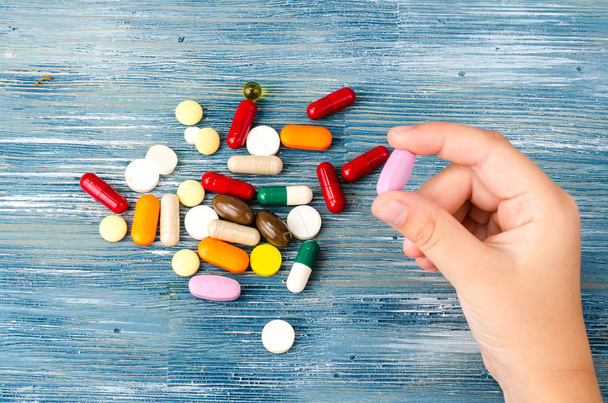 Vícebarevné pilulky, kapsle v ruce na modrém pozadí - Fotografie, Obrázek