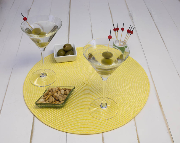 zwei Wodka Martinis in Gläsern mit Oliven und Snacks auf einem Tischset, Vorderansicht. - Foto, Bild