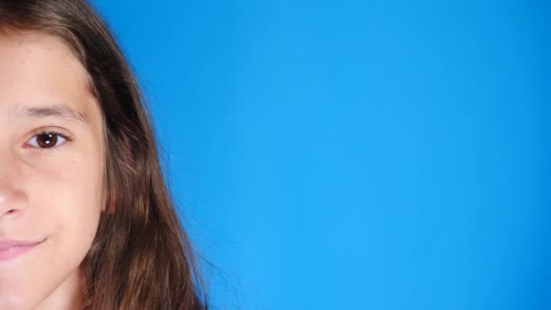 Portrait of cute excited attractive girl with long hair. laughing while standing on blue background. 4k, slow-motion, close-up, half face - Felvétel, videó