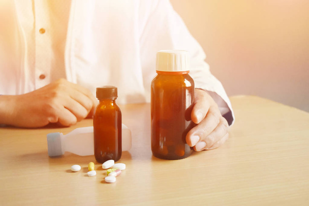 sfondo in luce calda asiatico uomo medico holding un bottiglia di pillole su un marrone tavolo e vuoto spazio per testo
. - Foto, immagini