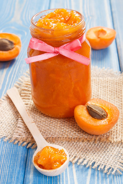 Apricot jam or marmalade in glass jar and ripe fruits on blue boards, concept of healthy sweet dessert - Foto, Bild