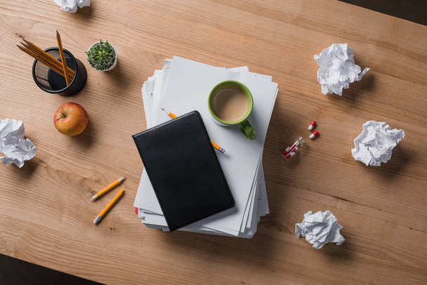 felülnézet halmozott üres papírok, csésze kávé és a notebook a tetején a fából készült asztal - Fotó, kép