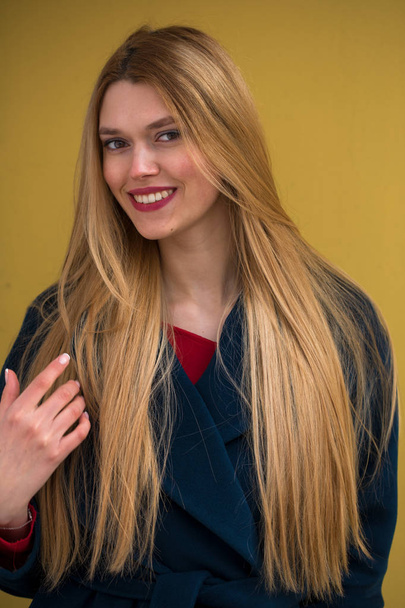Portrait of a young beautiful woman in blue coat, Happy blonde model against the yellow wall - Foto, afbeelding