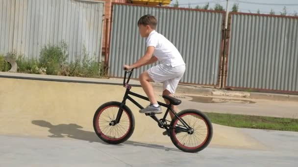 A boy is riding BMX cycling tricks in a skateboard park on a sunny day. Super Slow Motion - Filmagem, Vídeo