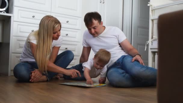 Uma família de três em camisetas brancas e jeans azuis sentados no chão de seu quarto brincando com o garoto em jogos intelectuais. Atirar em câmera lenta família feliz
 - Filmagem, Vídeo