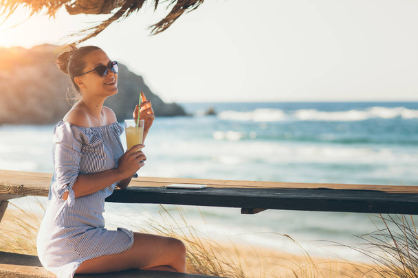 Pretty woman in summer dress drinking cocktail on beach - Foto, Imagen