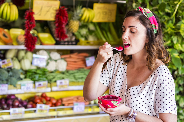 bella ragazza che assaggia un frutto del drago in una bancarella del mercato della frutta
. - Foto, immagini